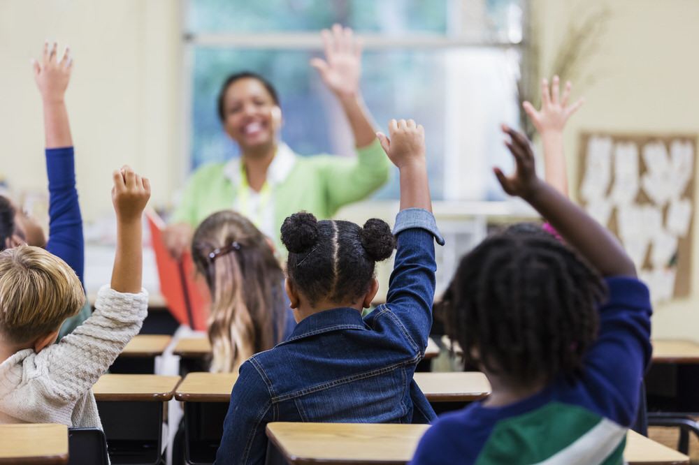 Teacher kids hands raised classroom Getty Images 1196756099